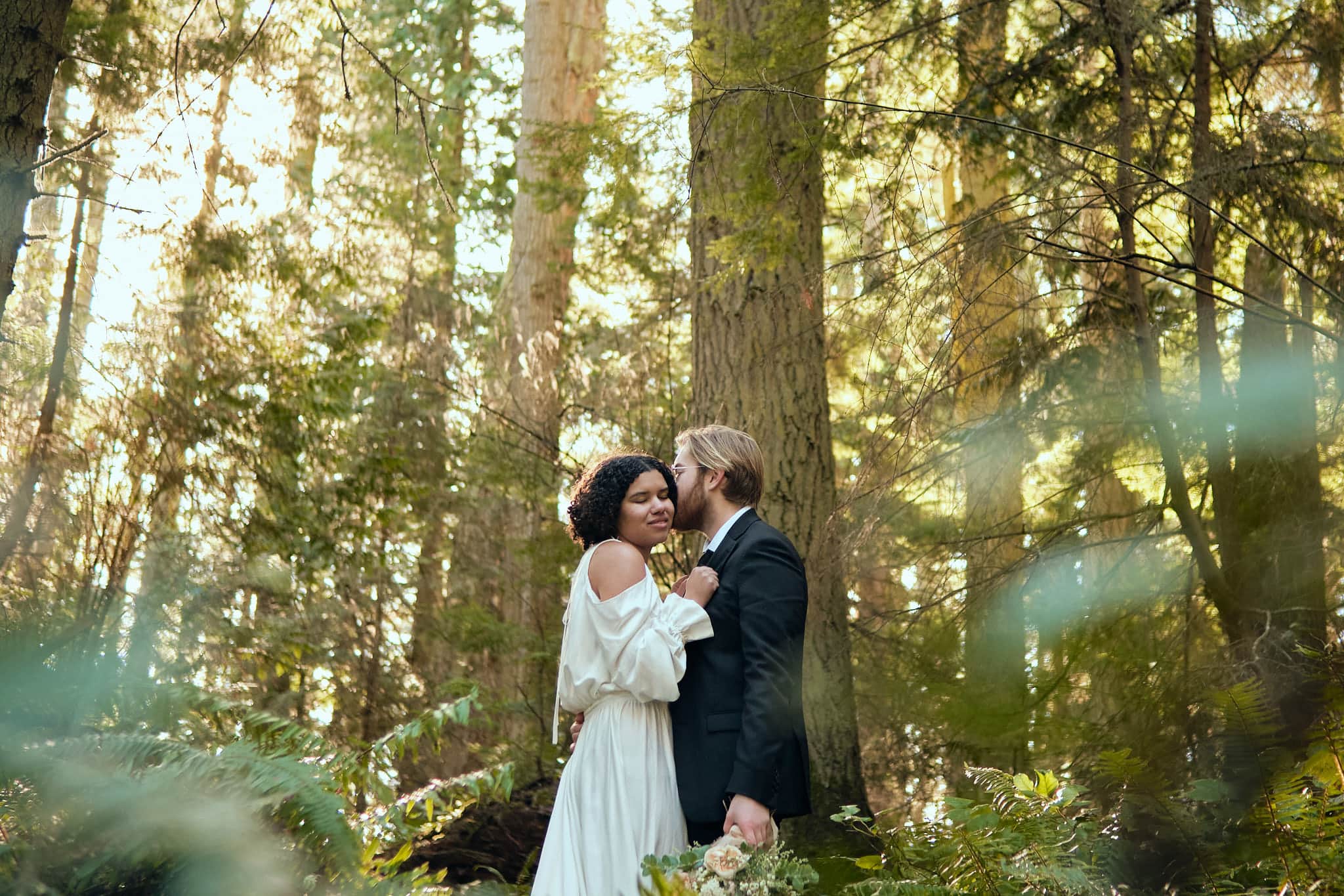 couple embraces as sun filters through evergreen trees