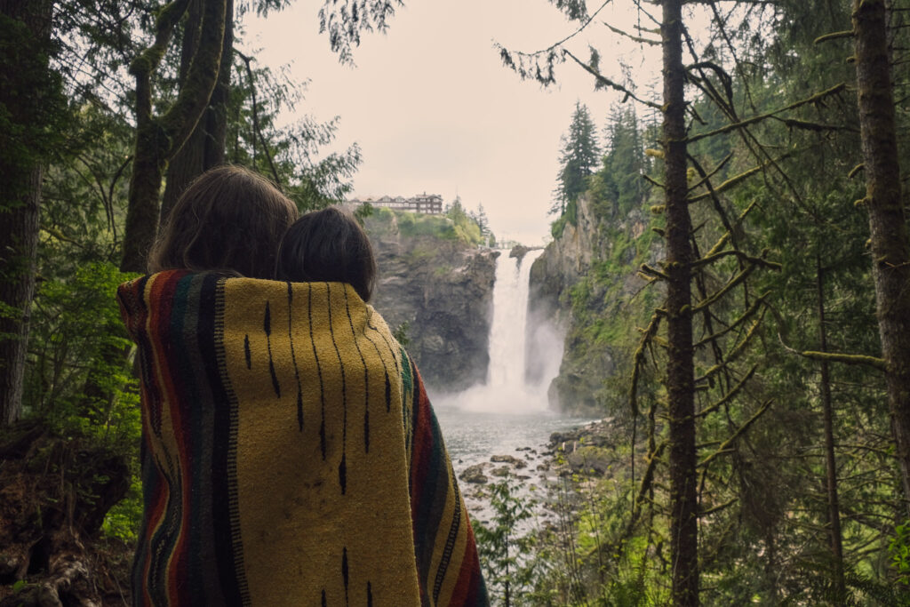 Two brides huddle under a blanket after their Washington waterfall elopement