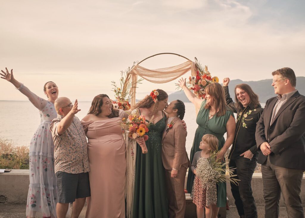 a group of friends cheer as two brides kiss