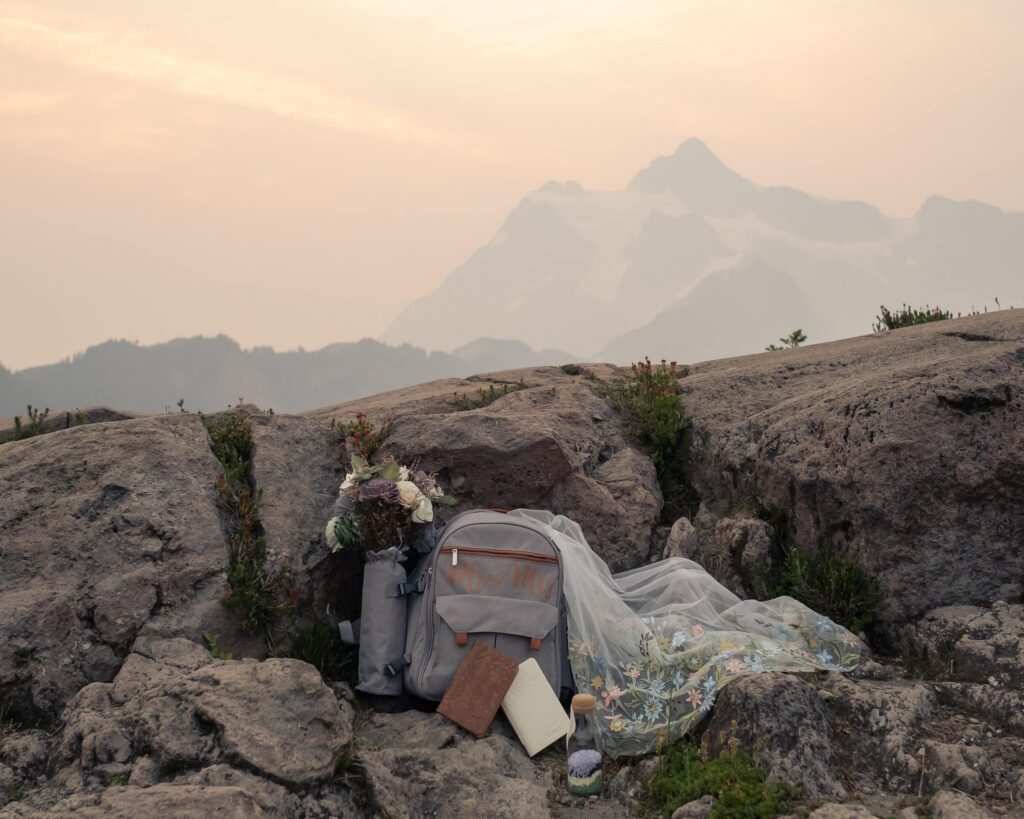 vow books, flowers and veil flows out of a backpack with a mountain backdrop